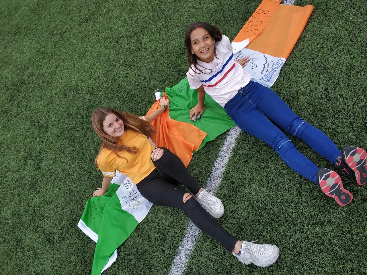 Jornada de deportes con bandera irlandesa Dos alumnas con la bandera de Irlanda en el campo de deportes del campamento de verano