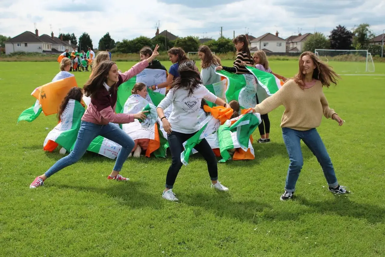 Juegos de equipo en el campamento de verano Alumnos jugando con banderas de Irlanda en el campo de hierba del campamento